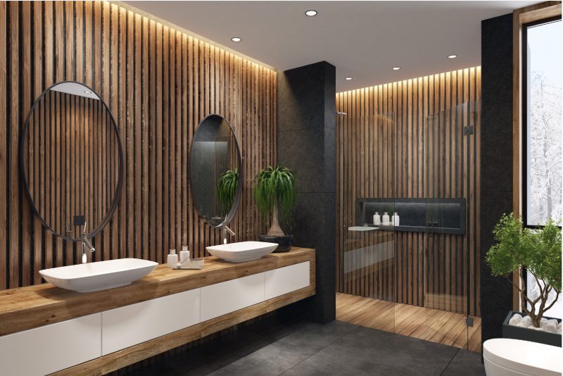 Modern bathroom with wooden panels, dual sinks, round mirrors, a large potted plant, and a glass-enclosed shower.