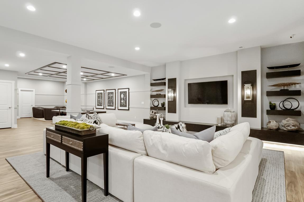 Spacious living room with a white sectional sofa, large wall-mounted TV, modern decor, and recessed lighting.