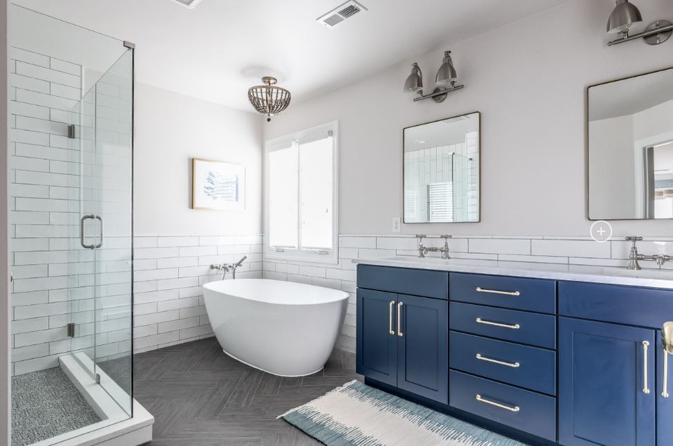 Modern bathroom with a freestanding tub, glass shower, white subway tiles, and blue vanity with double sinks.