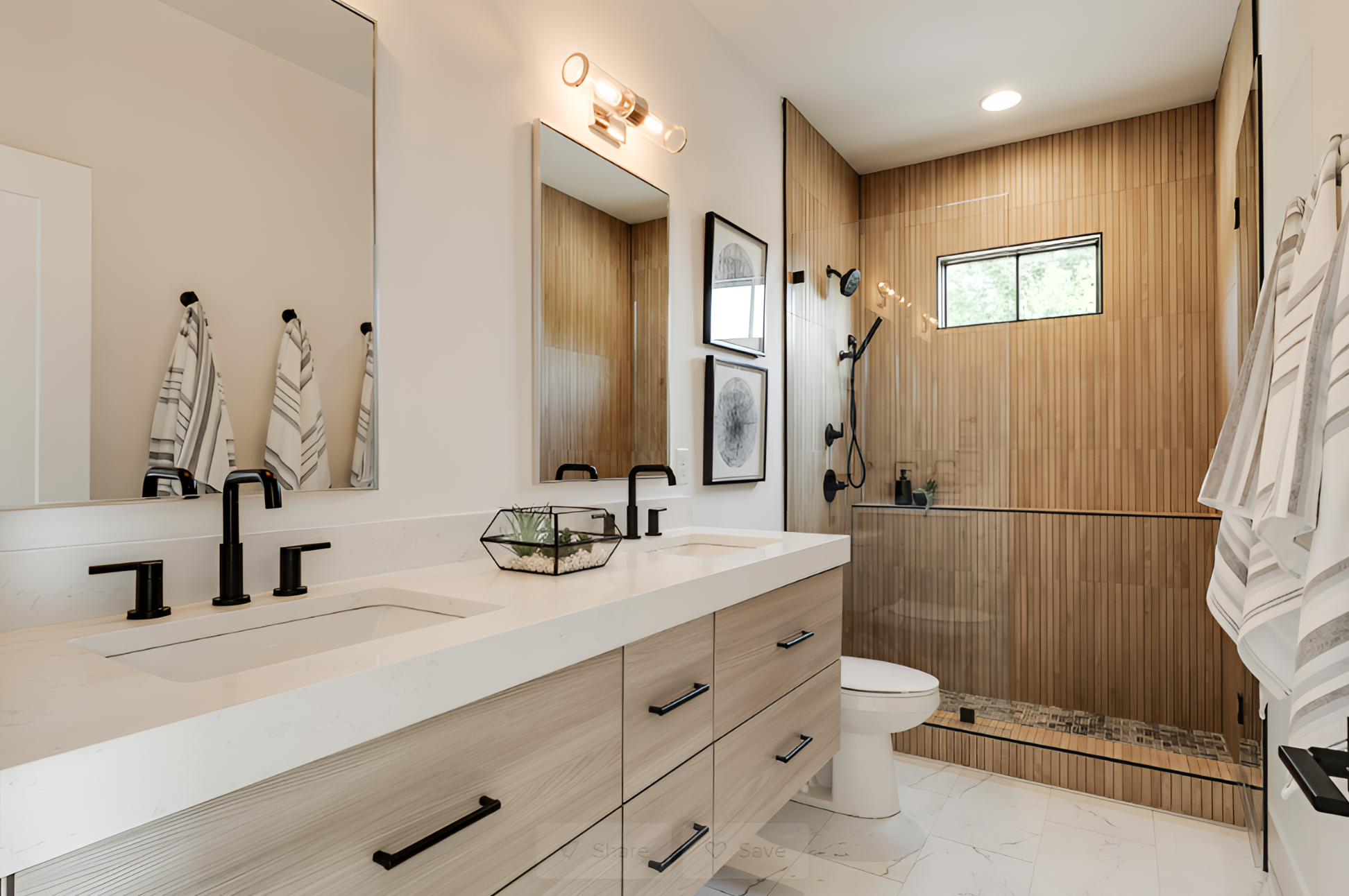 Modern bathroom with double sinks, black fixtures, and a wood-paneled shower. Two striped towels hang on the wall, and a small plant decorates the counter.