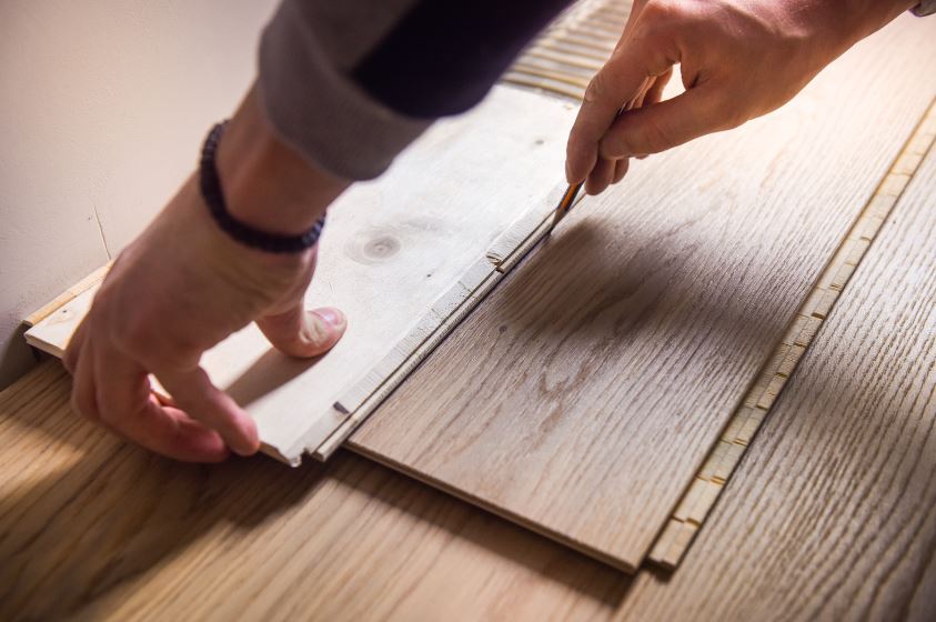 Hands laying wooden flooring with a guide tool, adjusting planks into place.