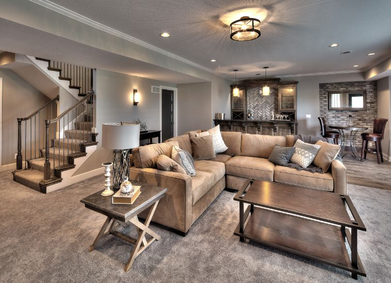 Spacious living room with a large beige sectional sofa, wooden coffee table, staircase, and modern bar area in the background.