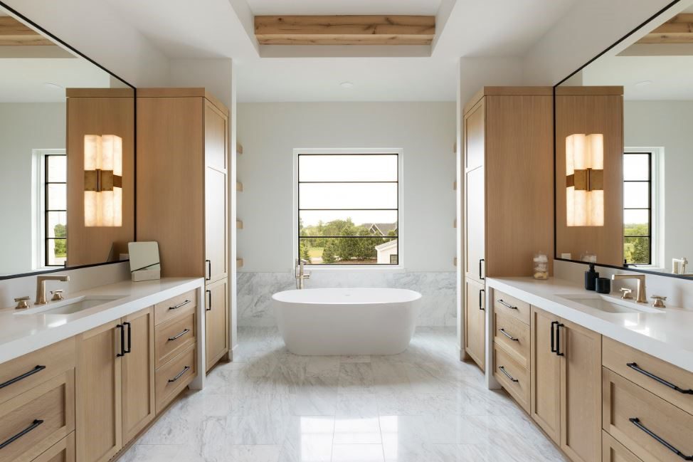 Modern bathroom with wooden cabinets, a freestanding bathtub, and large windows. White marble floor and neutral tones create an elegant atmosphere.