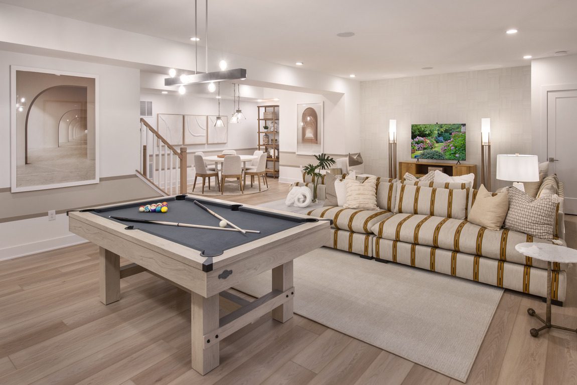 A modern living room with a striped sofa, a pool table, and a mounted TV. A dining area is visible in the background, and artwork decorates the walls.